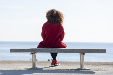 a woman sitting alone on a bench in front of the ocean