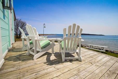 Three white adirondac chairs on a deck overlooking the bay