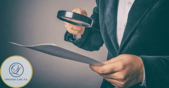 image of man in suit holding a magnifying glass to paper.