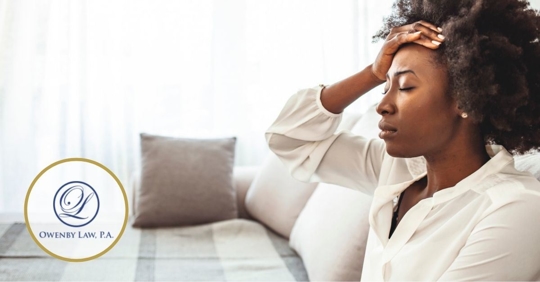 African American woman sitting by a window with her hand on her forehead.