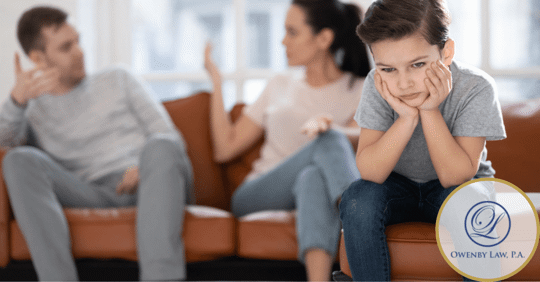 Image of parents sitting on a couch in the background having a conversation with a child in the front of the photo with his head in his hands.