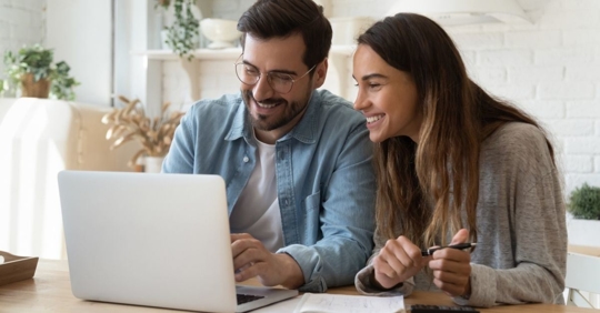 young couple smiling and looking at a laptop